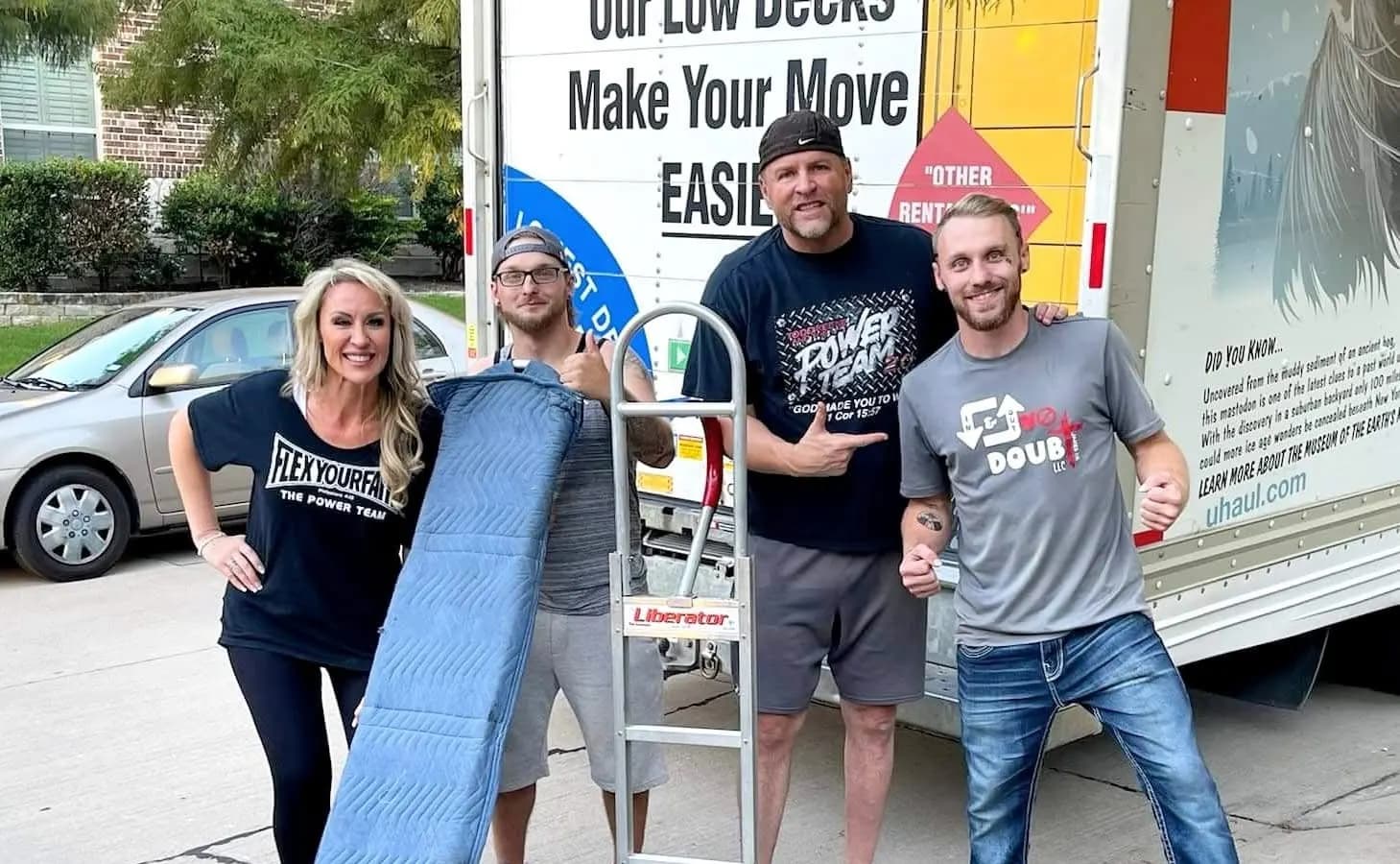 Four cheerful In & Out No Doubt movers posing with a hand truck in front of a U-Haul truck
