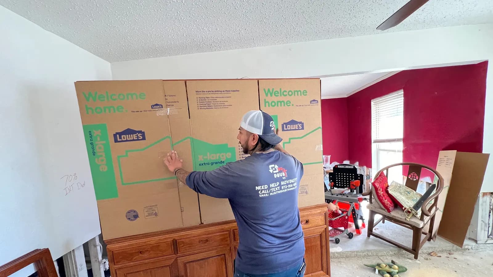 Mover in an In & Out No Doubt shirt boxing up a wood sideboard with extra-large moving boxes