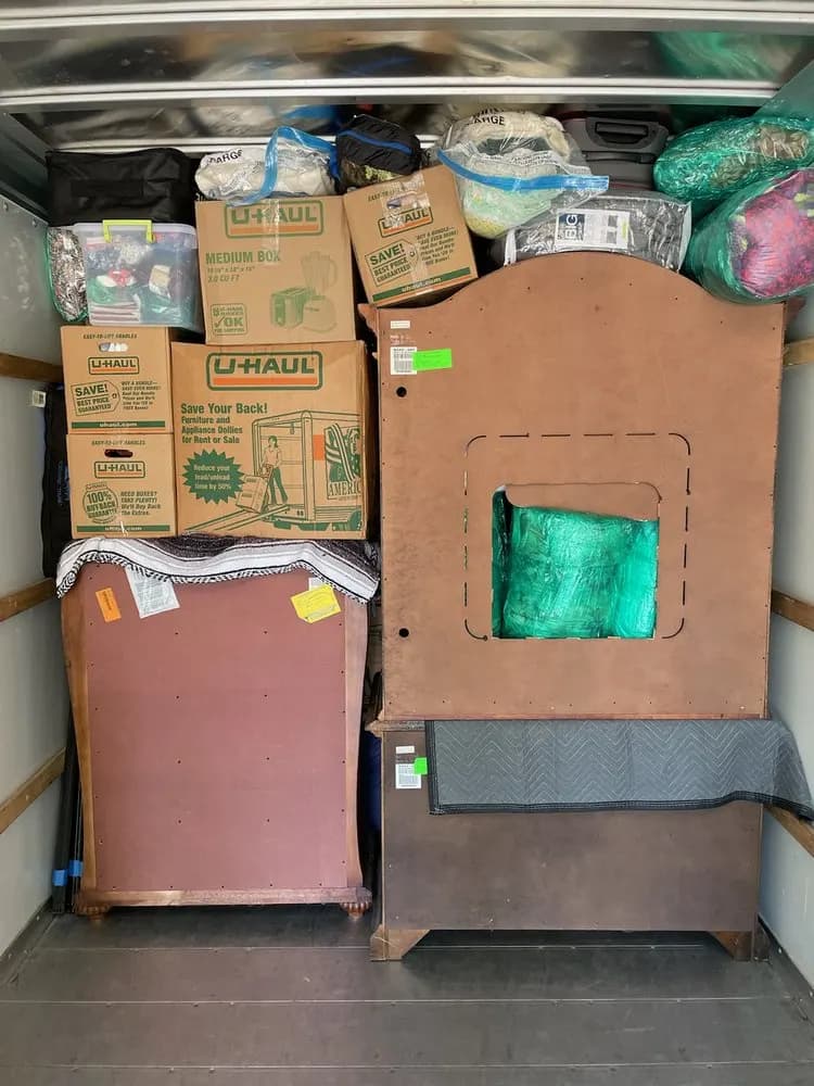Dressers and a headboard padded with blankets and loaded beside moving boxes in a truck