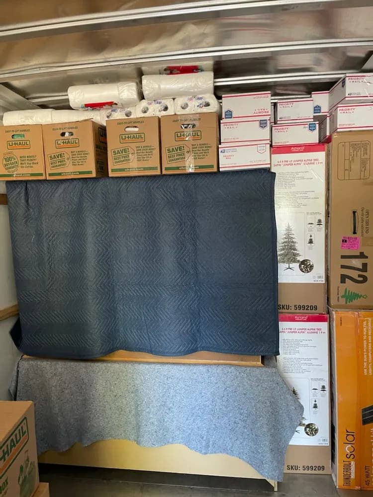Furniture wrapped in moving blankets below stacked boxes in a moving truck
