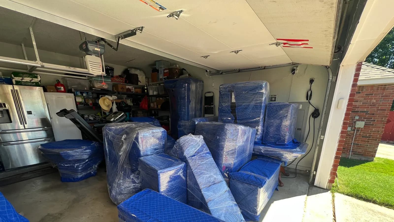 Furniture wrapped in moving blankets and stretch wrap, staged in a garage before loading