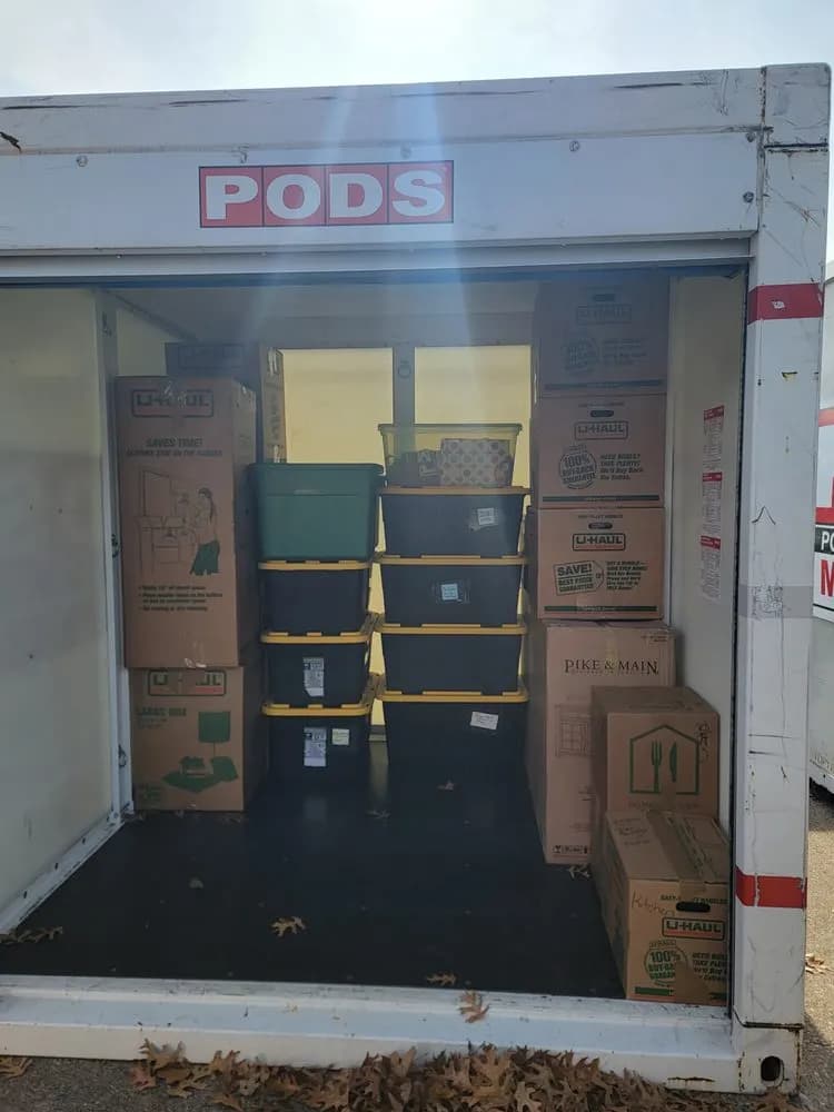 Open portable storage container packed with moving boxes and stacked storage totes