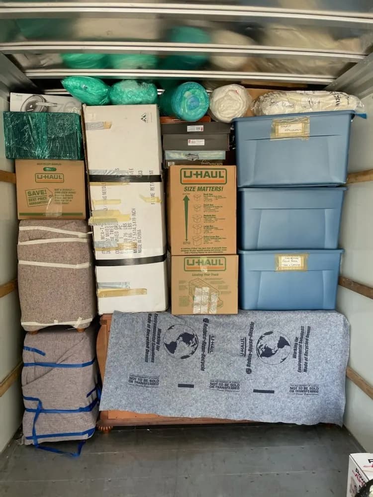 Neatly packed moving truck with stacked boxes, labeled blue totes, and blanket-wrapped furniture