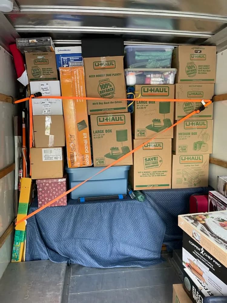 Moving boxes stacked and secured with orange ratchet straps inside a loaded moving truck