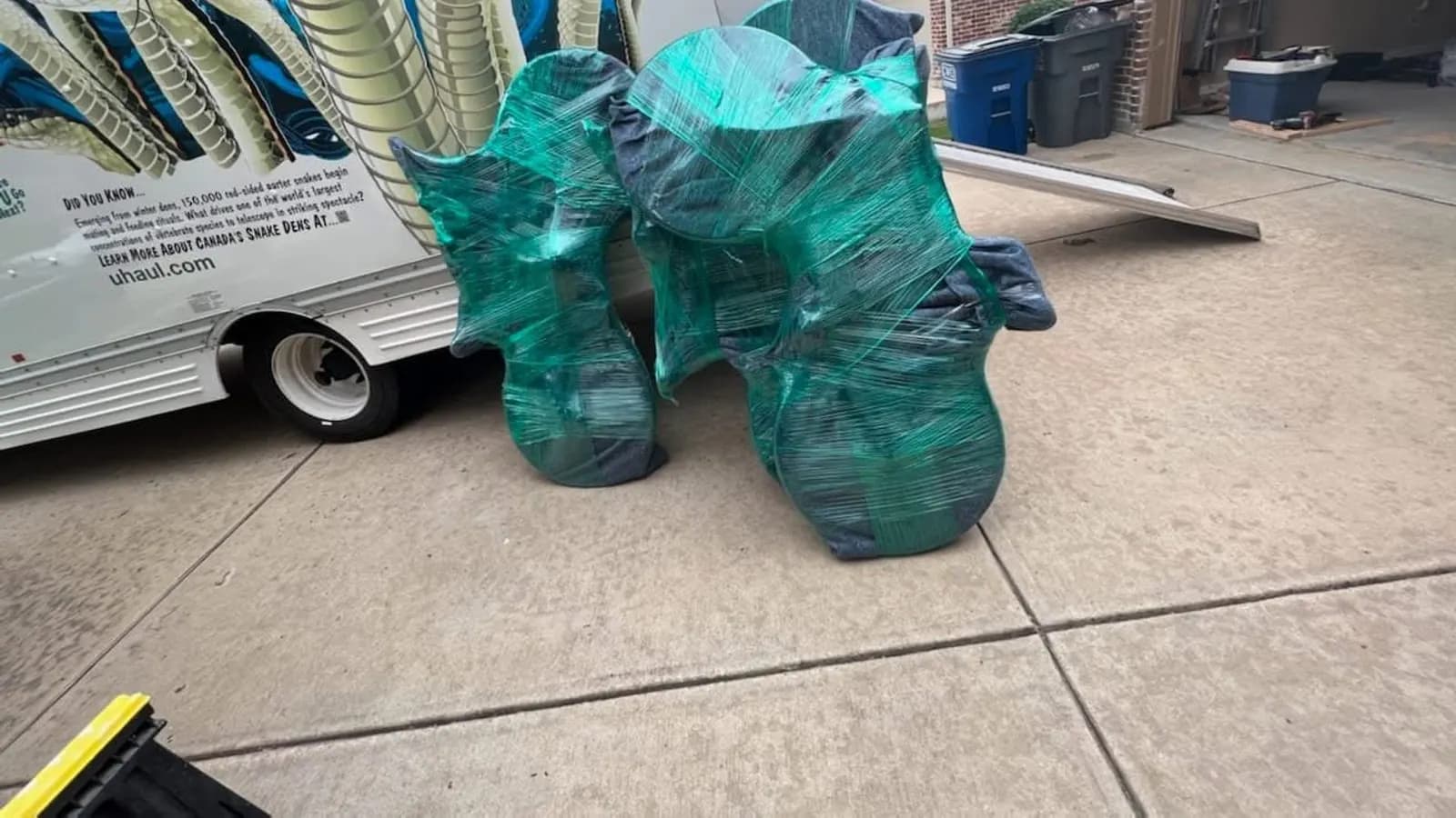 Furniture padded in blankets and wrapped in stretch film staged on a driveway beside a moving truck