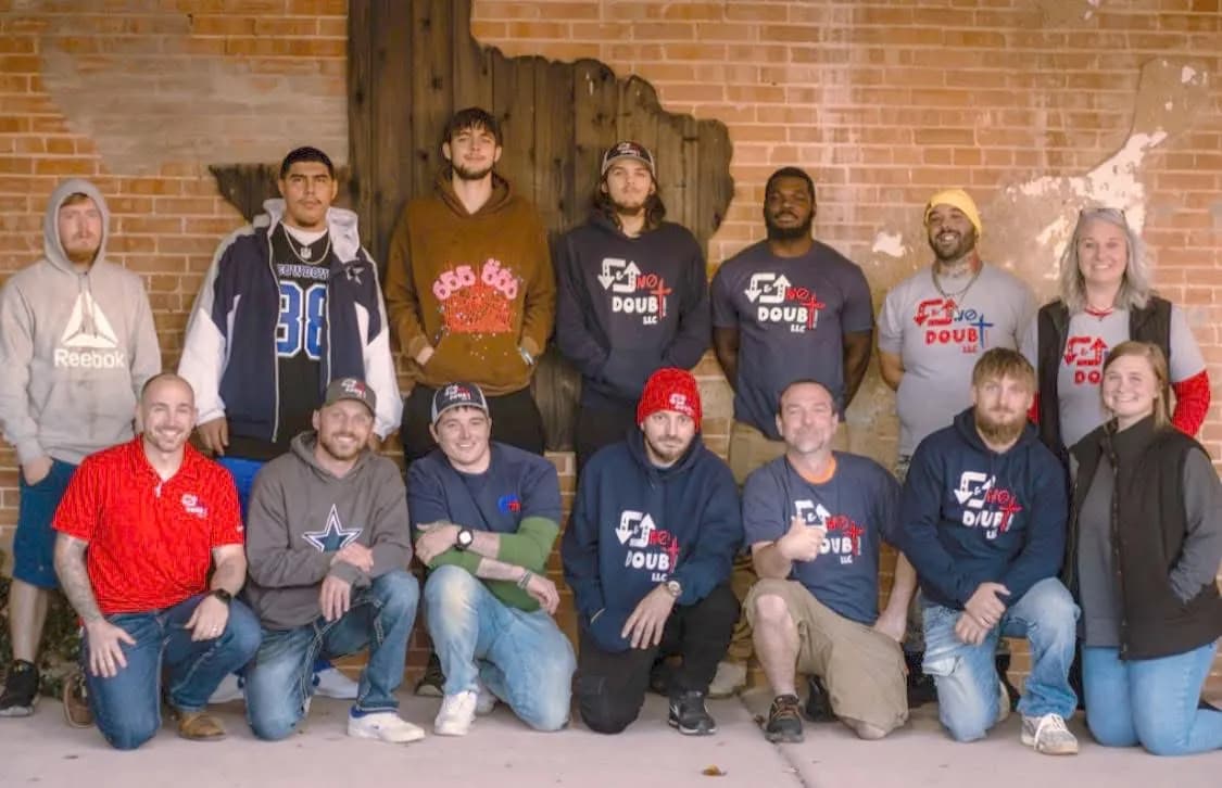 The In & Out No Doubt team in logo shirts, posed by a wooden Texas cutout on a brick wall